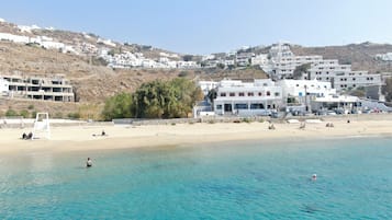 A coastal town with white buildings, a sandy beach, and clear blue waters.