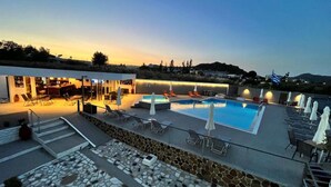 Et tag med swimmingpool, liggestole, parasoller, et barområde og udsigt over det omkringliggende landskab.