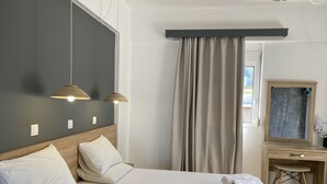 Et hotelværelse med to senge, et skrivebord, en stol, et spejl og et vindue med gardiner.