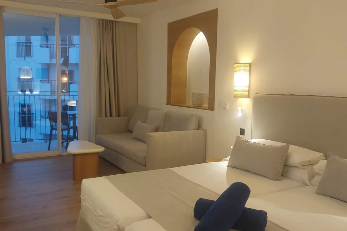 Ein Hotelzimmer mit Bett, einer Couch, einem kleinen Tisch und einem Balkon mit Blick auf Gebäude.