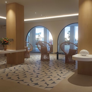 Un hall con suelo estampado, sillas de mimbre y una recepción con un jarrón de flores.