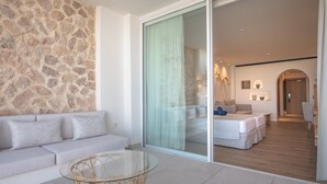 A modern hotel room with a stone wall, a glass door leading to a balcony, a sofa, a glass table, and a bed with a view. - Blau Park (Sant Antoni de Portmany)