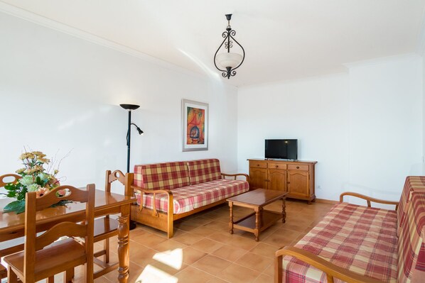 Una sala de estar con un sofá de madera, una mesa de madera, un mueble para la televisión y una lámpara de pie.