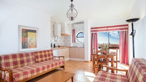 En stue med sofa og spisebord, et køkken med et vindue, og udsigt over byen.