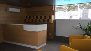 A reception desk with a wooden finish and a white counter, a set of numbered blocks above it, and two yellow chairs in the foreground. - Puerto Principe Apartments (PUERTO RICO)
