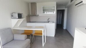 A compact living space with a kitchenette, a dining area with a white table and two chairs, and a grey sofa. - Puerto Principe Apartments (PUERTO RICO)