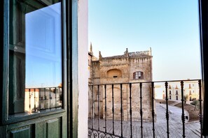 Un balcón con barandilla de hierro forjado que da a un edificio histórico de piedra con ventanas de arco y elementos decorativos.