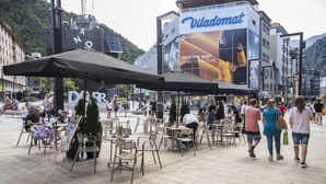 An outdoor café area with tables and chairs, a large Viladomat advertisement, and a mountainous backdrop. - Valmar (Andorra la Vella)