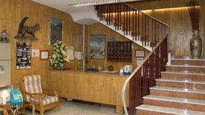 A reception area with a wooden desk, a chair, a staircase, and a vase on the wall. - Valmar (Andorra la Vella)