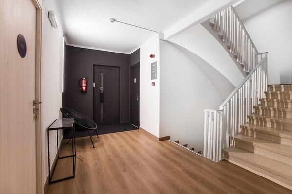 A modern interior with a wooden floor, a staircase with white railings, a black chair, and a small table. - Valmar (Andorra la Vella)