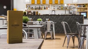 A modern cafe interior with a wooden table, metal chairs, and a brick wall. There are shelves with bottles and a menu stand. - Valmar (Andorra la Vella)