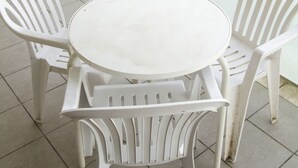 Un balcón con una mesa redonda y dos sillas blancas de plástico.