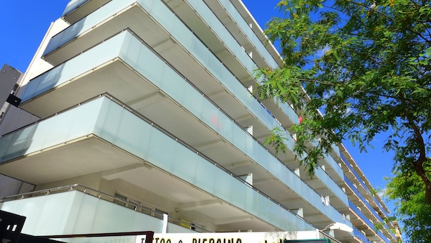 Un edificio de varios pisos con un diseño arquitectónico moderno, que cuenta con una serie de balcones y fachada de vidrio.