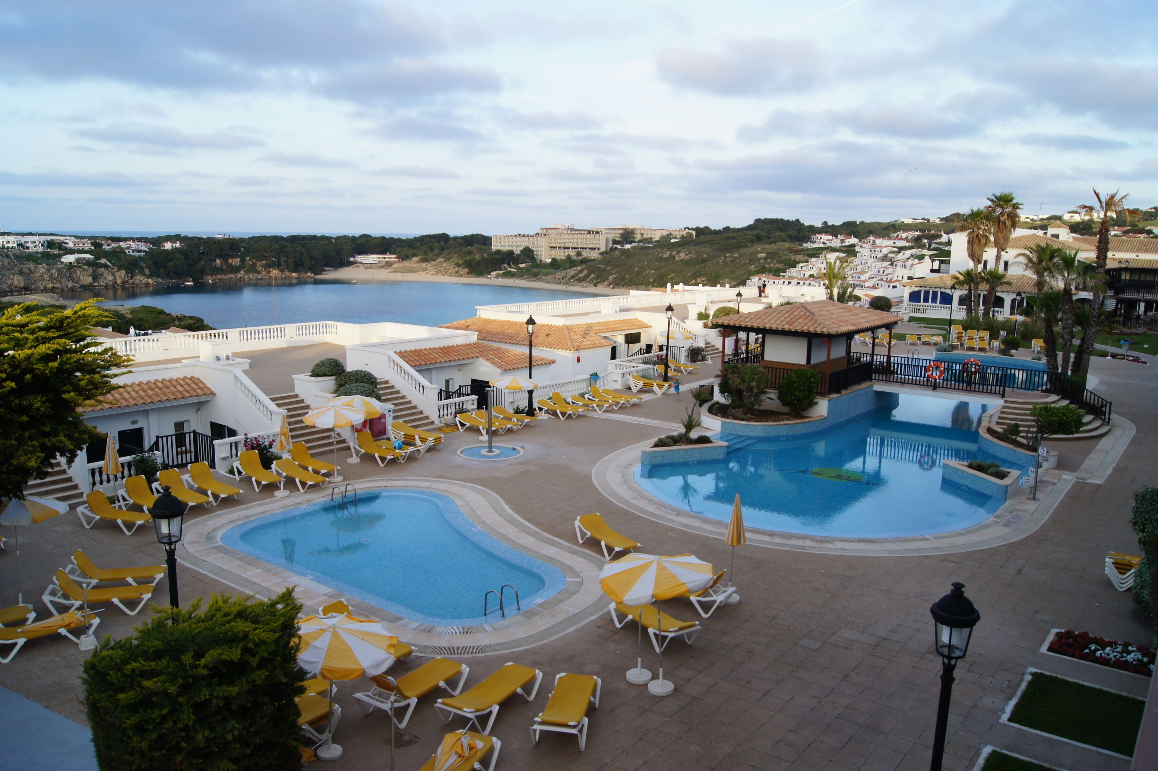 Un resort con dos piscinas, tumbonas y vista al mar.
