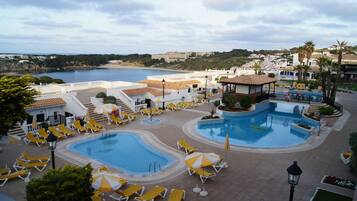 Un resort con dos piscinas, tumbonas y vista al mar.