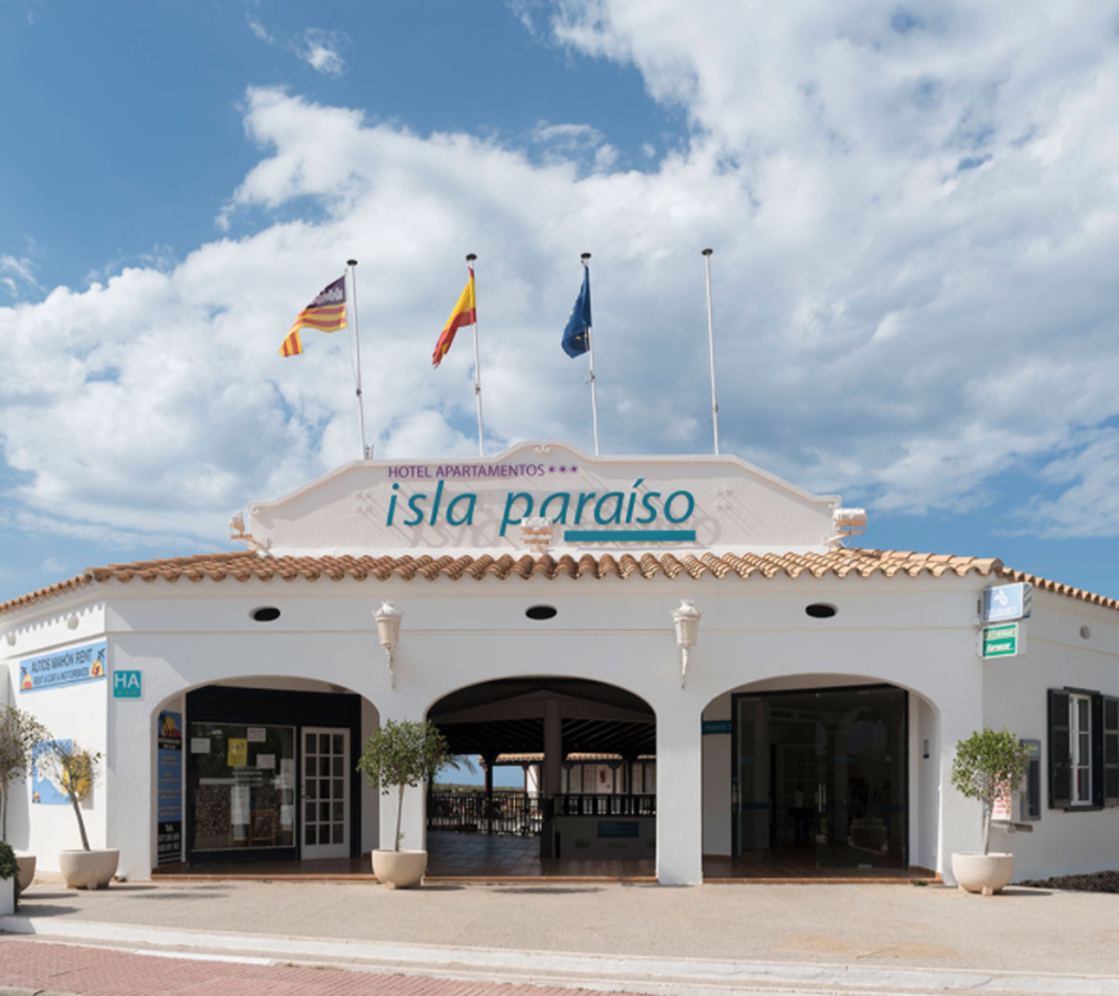 Un hôtel appelé « Isla Paraíso », doté d’un toit en tuiles, de deux arches à l’entrée et de drapeaux au sommet.