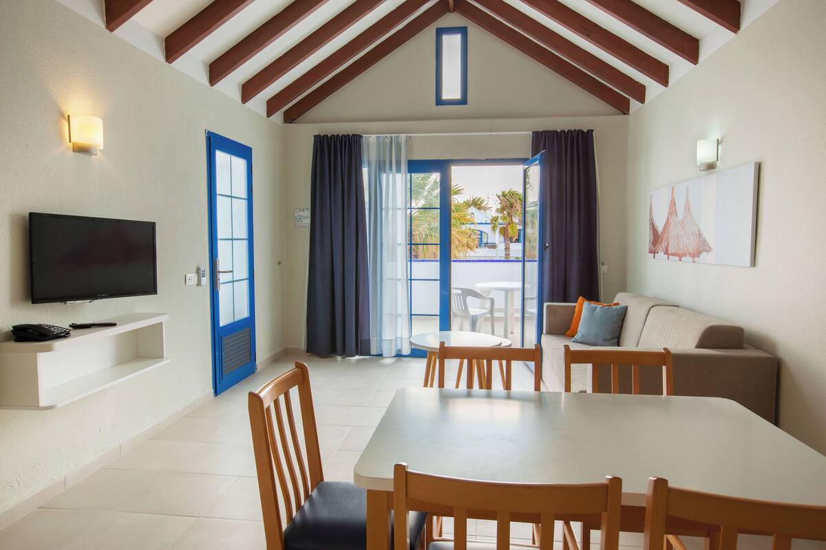 Un comedor con una mesa y sillas, un televisor en un estante y un sofá.