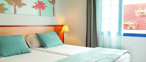 Ein Hotelzimmer mit zwei Betten, türkisblau gestreuter Bettwäsche, einer Wandmalerei von Palmen, einem Fenster mit Vorhängen und Blick auf einen rot-weißen Bereich im Freien.