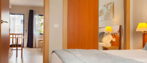 Una camera d'albergo con un letto, due lampade ai comodini, un armadio in legno, una sedia e una scrivania.