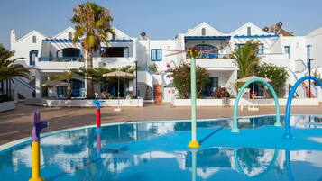 Area piscina con giochi colorati, una piscina blu cristallina e un edificio bianco con dettagli e balconi blu.