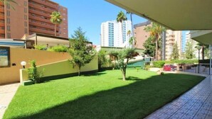 A courtyard with a well-maintained lawn, a small tree, and a building in the background. - Europa Center (Benidorm)