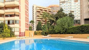 A swimming pool with lounge chairs, surrounded by greenery and tall buildings. - Europa Center (Benidorm)