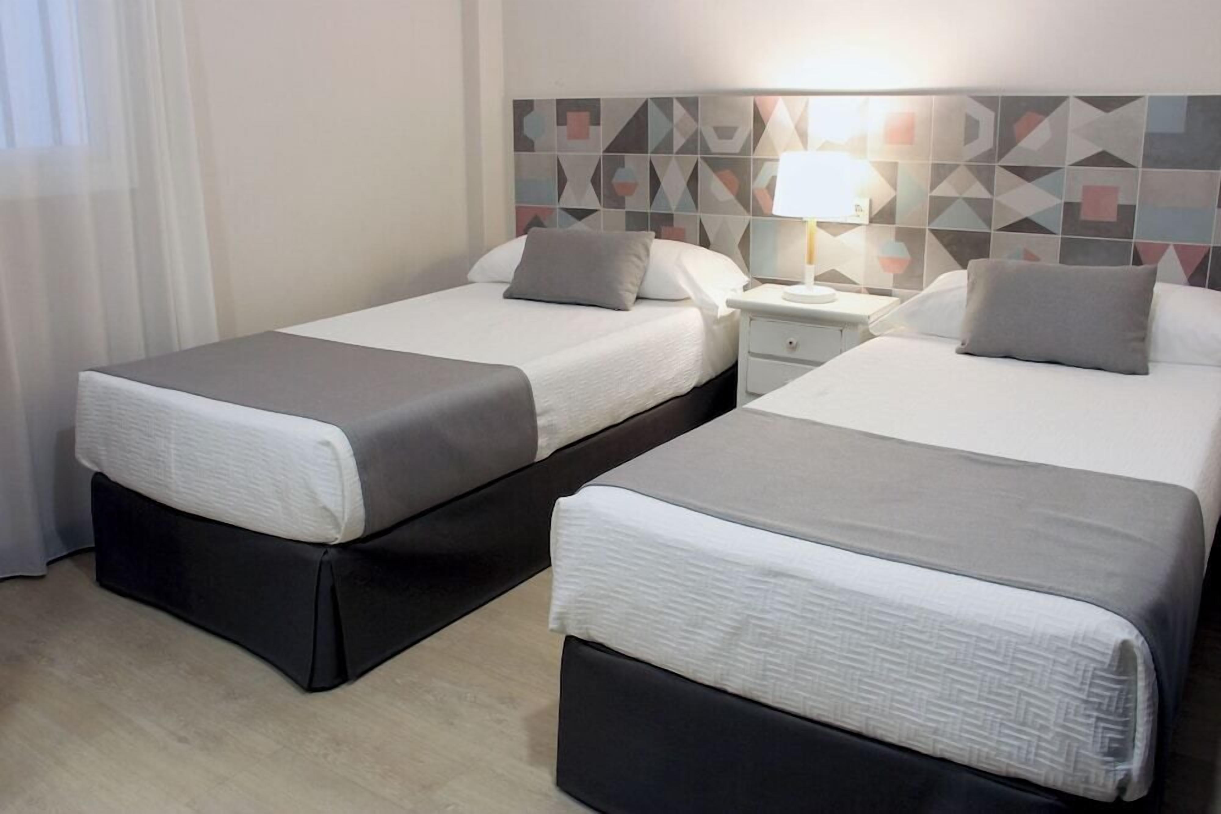 Two twin beds with black bases, a nightstand with a lamp, and a geometric-patterned wall.