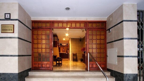Entrada de un hotel con una escalera de mármol, puertas de madera y un letrero que dice 'Apartamentos Ribera'.