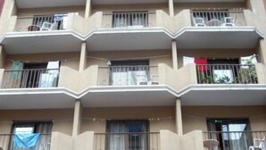 Un edificio de varios pisos con balcones, cada uno con barandilla metálica, una mesa y una silla.