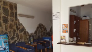 Una zona de recepció amb parets de pedra, cadires blaves, una taquilla de fusta i un quadre de rodes.