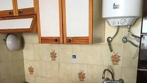 Una cuina reduïda amb armaris de fusta, un sol d'integrat i un frigorífic compacte.