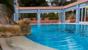 Una piscina con una formación rocosa y una zona cubierta con puertas de cristal.