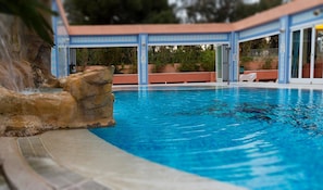 A swimming pool with a rock feature and a covered area with glass doors. - Tropic Relax (Finestrat)