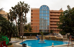 Un hotel con piscina, palmeras y un edificio grande con un ventanal en forma de cúpula azul.