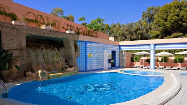 Una piscina con pared de roca, sillas de descanso y sombrillas.