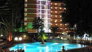 Un hotel con piscina, palmeras y una fachada iluminada.