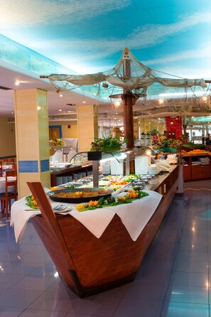 A buffet setup with a variety of food items, a decorative ceiling, and a polished floor. - Tropic Relax (Finestrat)