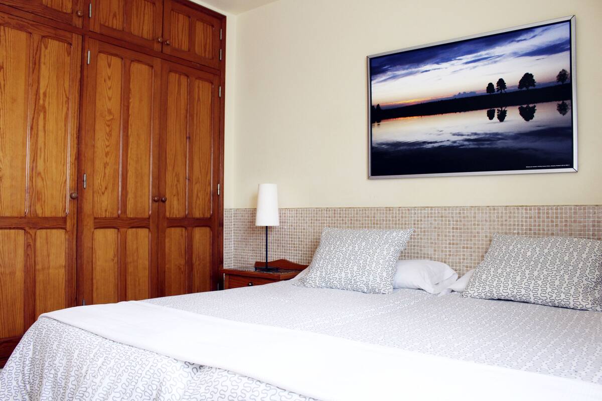Ein Hotelzimmer mit einem großen Bett, einem Holzschrank und einem Wandbild mit Sonnenuntergang über einem See.