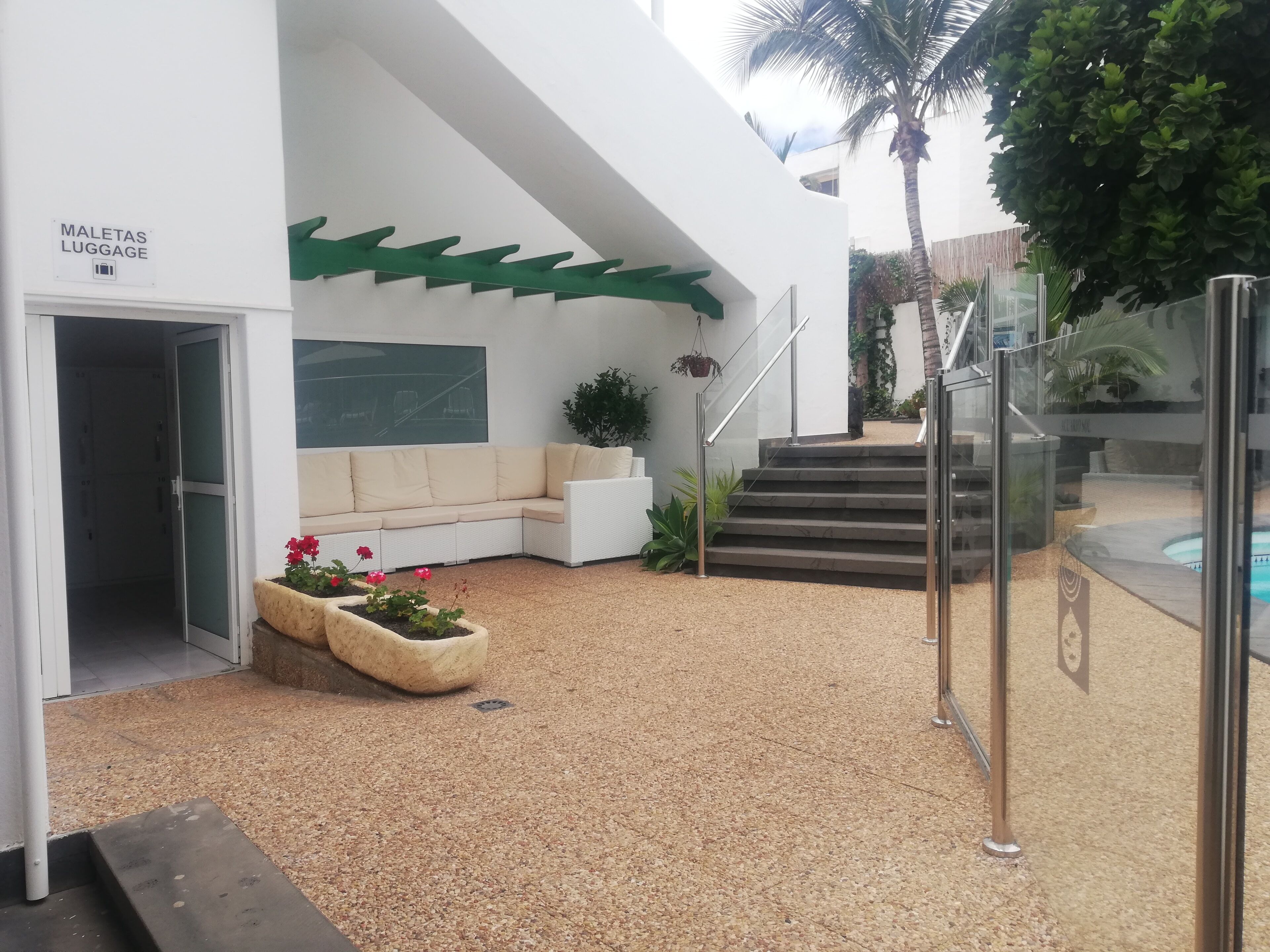 Un edificio moderno con fachada blanca, un área de descanso con cojines, una escalera y un letrero que dice "MALETAS LUGGAGE".
