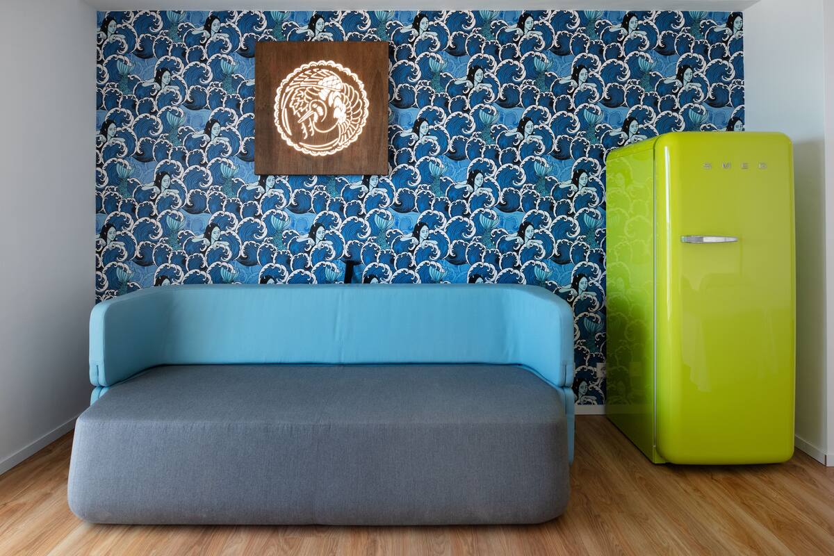 A room with a blue sofa, a green refrigerator, and a wall with a wave pattern.