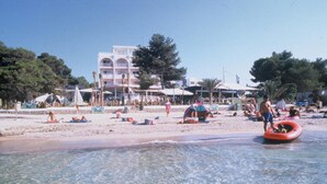 Une plage avec une eau claire, des gens qui prennent un bain de soleil et un bâtiment en arrière-plan.