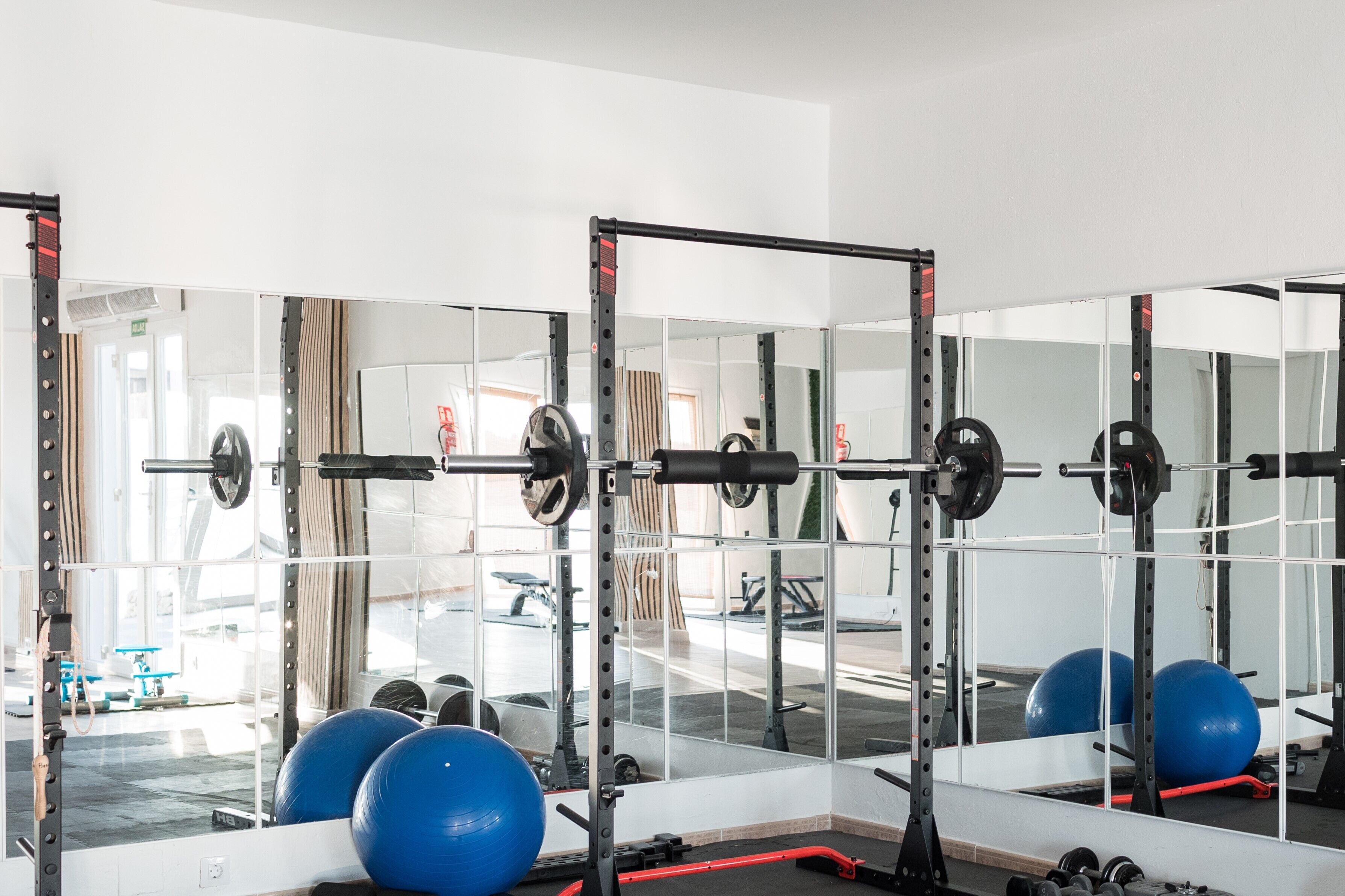 Un gimnasio con paredes espejadas, equipo de levantamiento de pesas y pelotas de ejercicio.