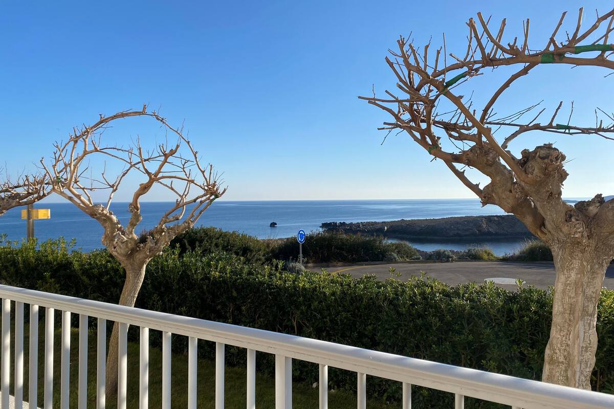 A balcony with a view of the sea, a road sign, and a white railing.