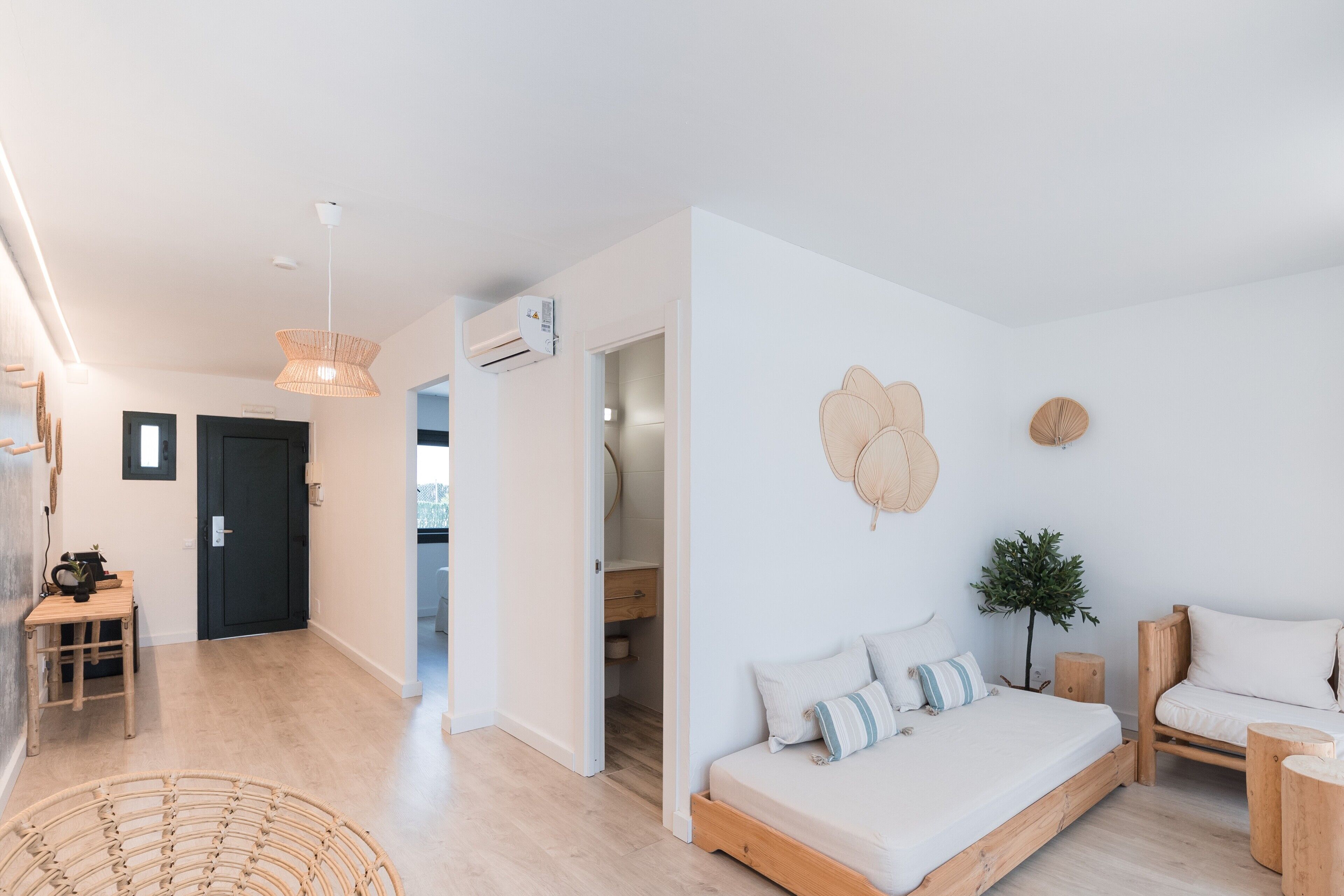A modern, minimalist bedroom with a wooden bed, a small bedside table, and a wall-mounted fan.
