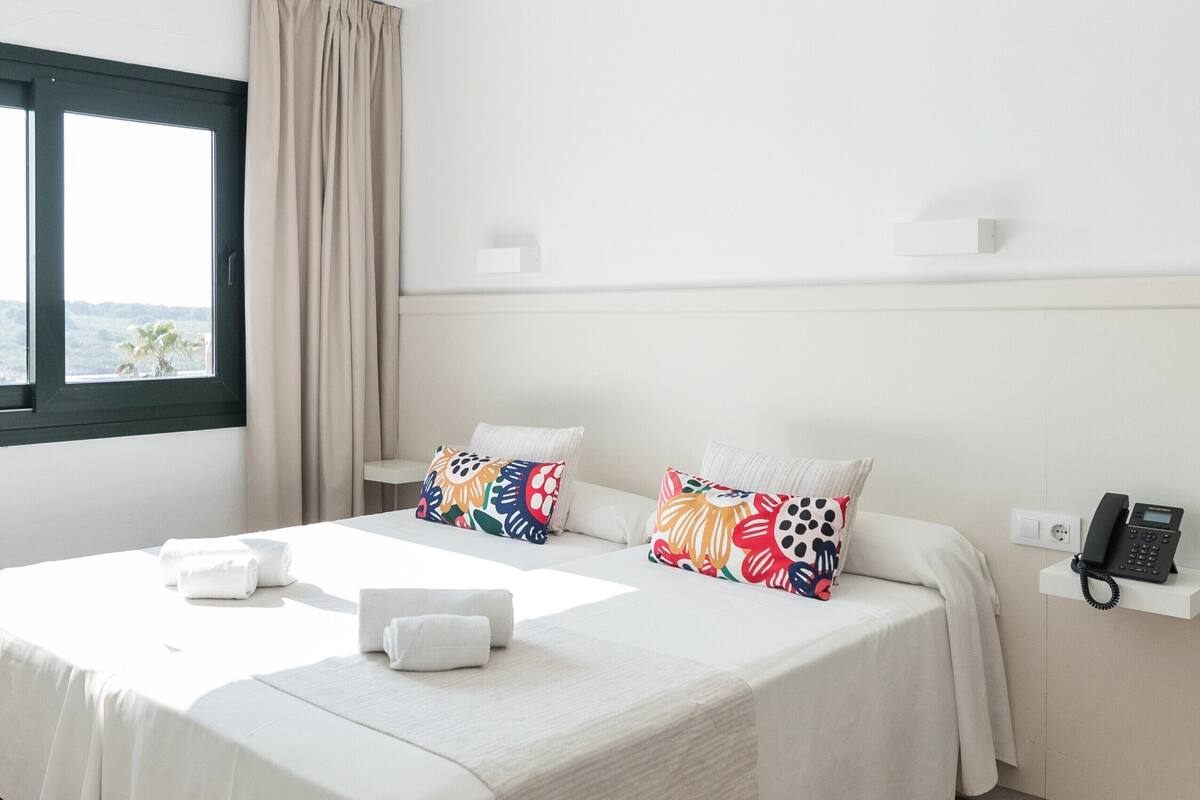A hotel room with two beds, a window with a view, a phone on a shelf, and a curtain.