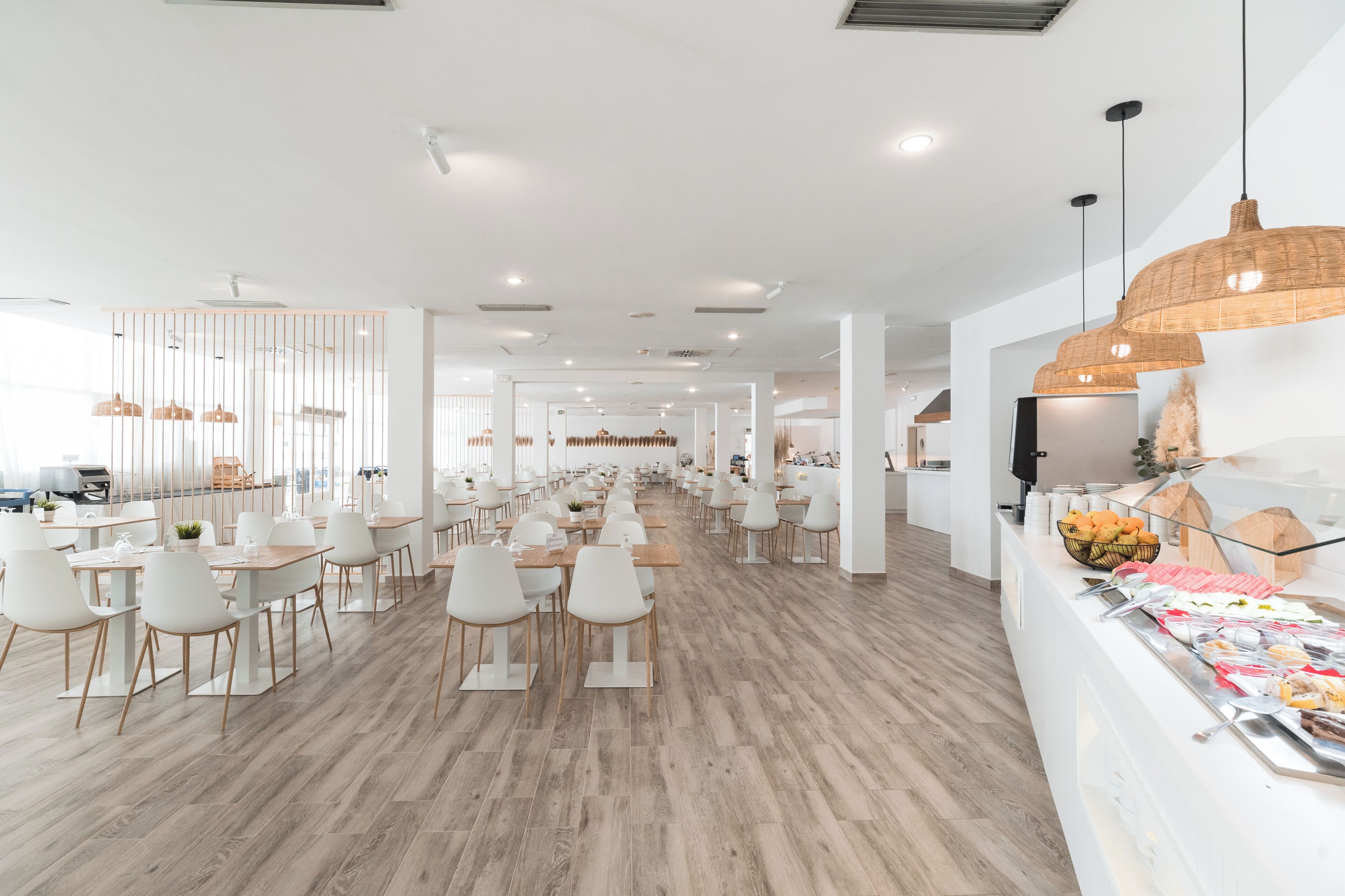 Un'ampia sala da pranzo con sedie e tavoli bianchi, un banco buffet con diverse pietanze e illuminazione a sospensione.