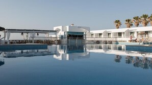 A pool area with a clear view of the pool, a covered seating area, and a building with a white facade. - Aparthotel Beach Club (Mercadal)