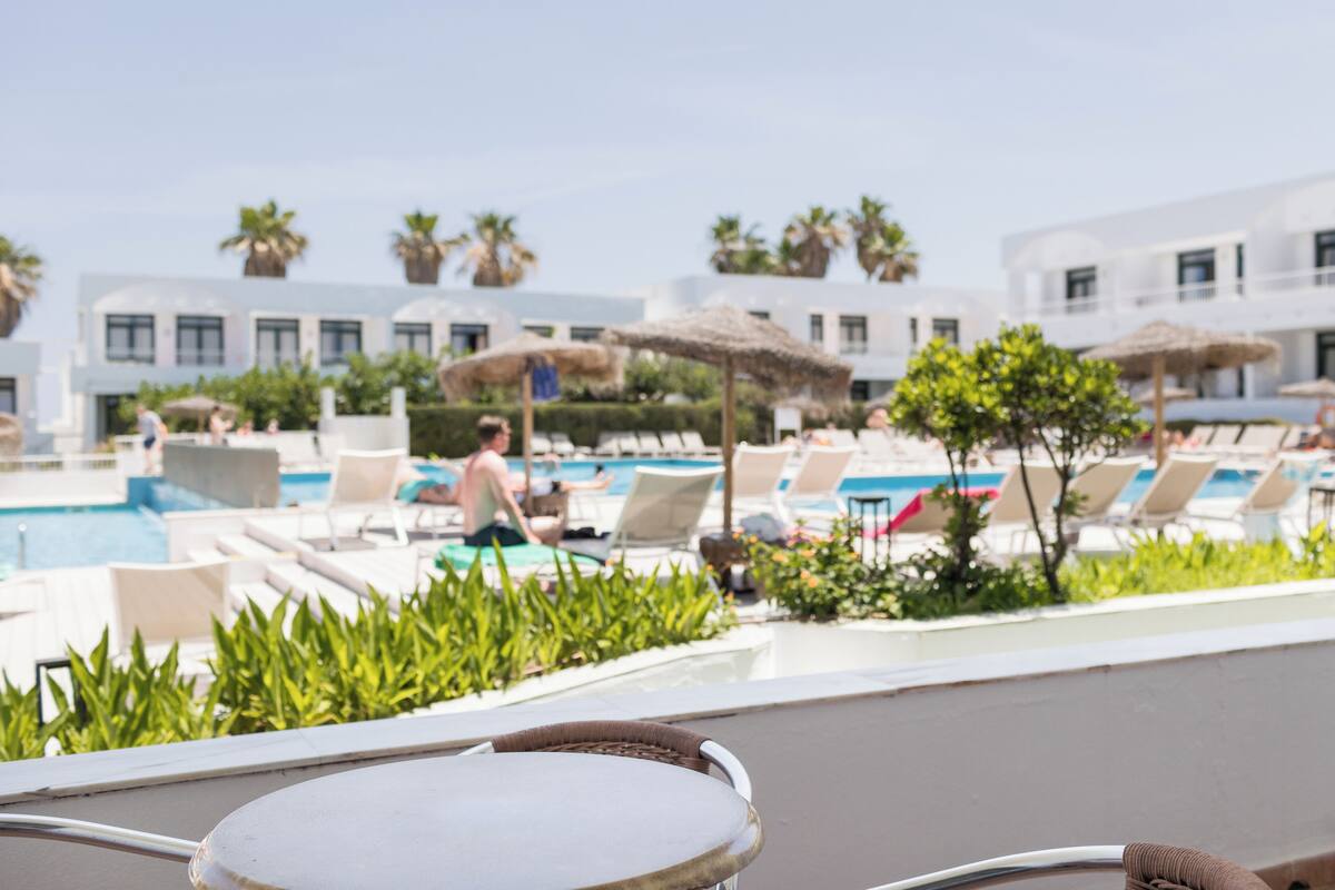 A poolside area with lounge chairs, a small pool, and a building with white walls and balconies.