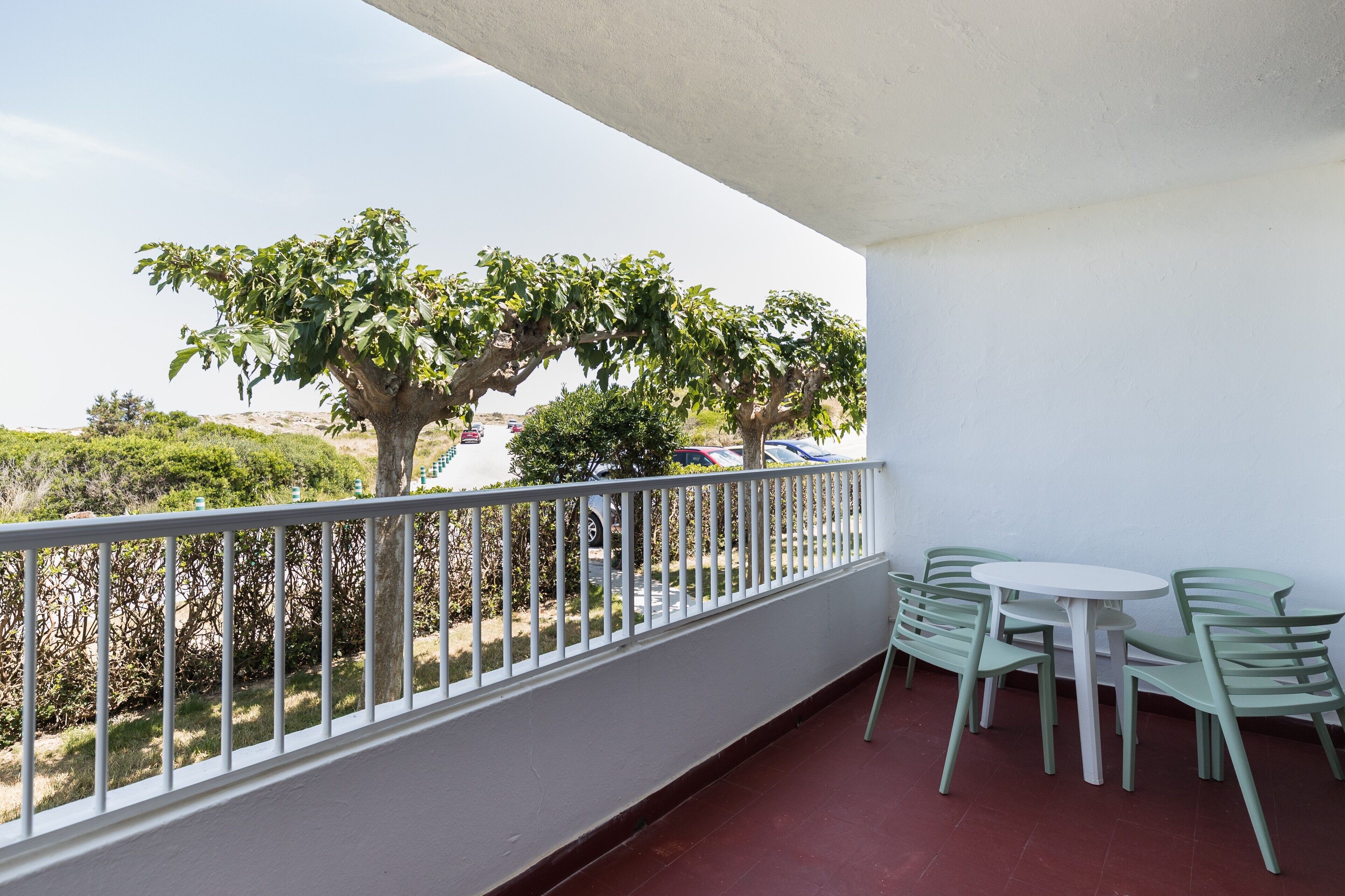 A balcony with a white railing, a small round table, and two green chairs.