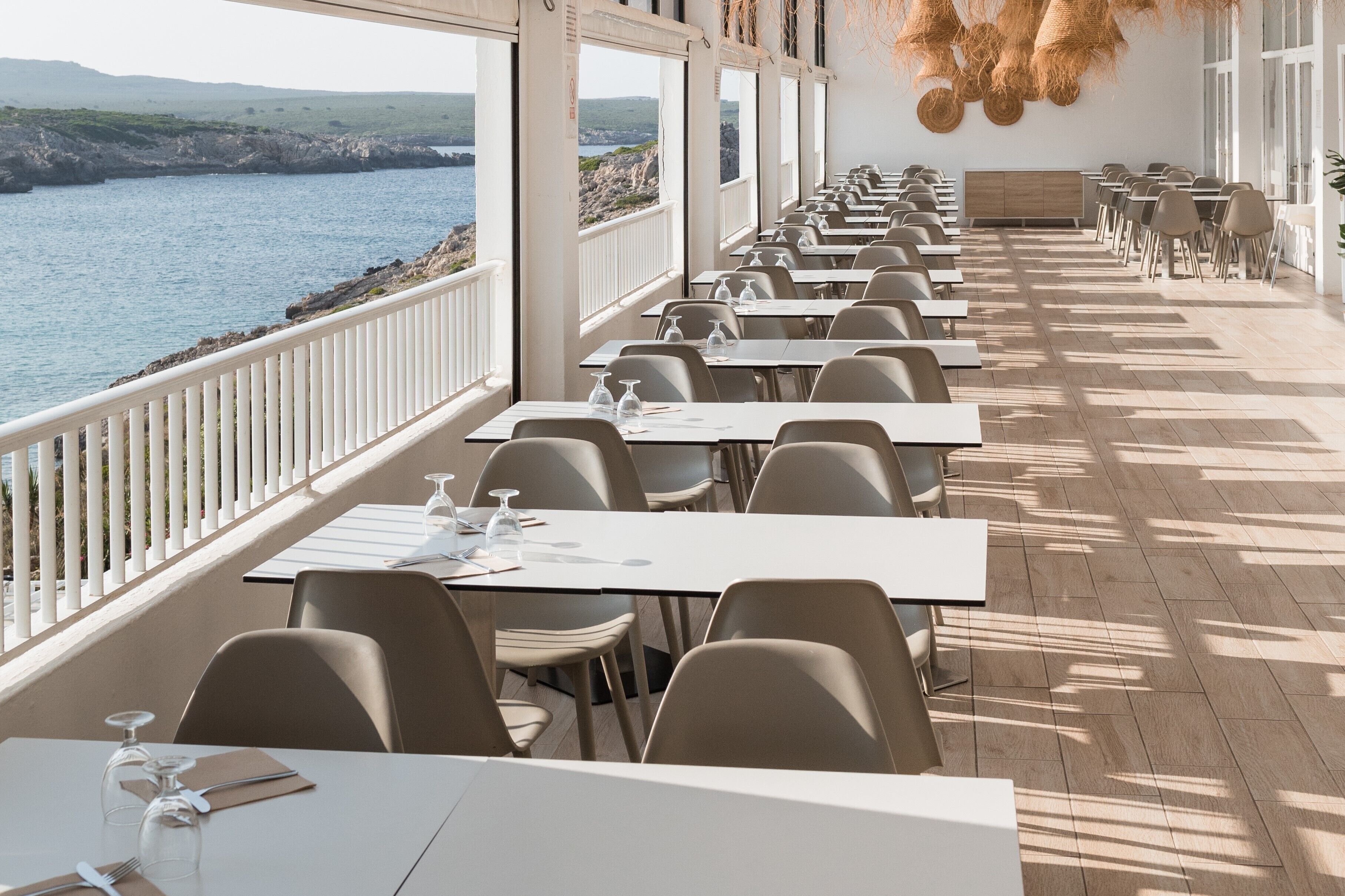 Un restaurante con mesas y sillas dispuestas a lo largo de un balcón con vista a un cuerpo de agua.